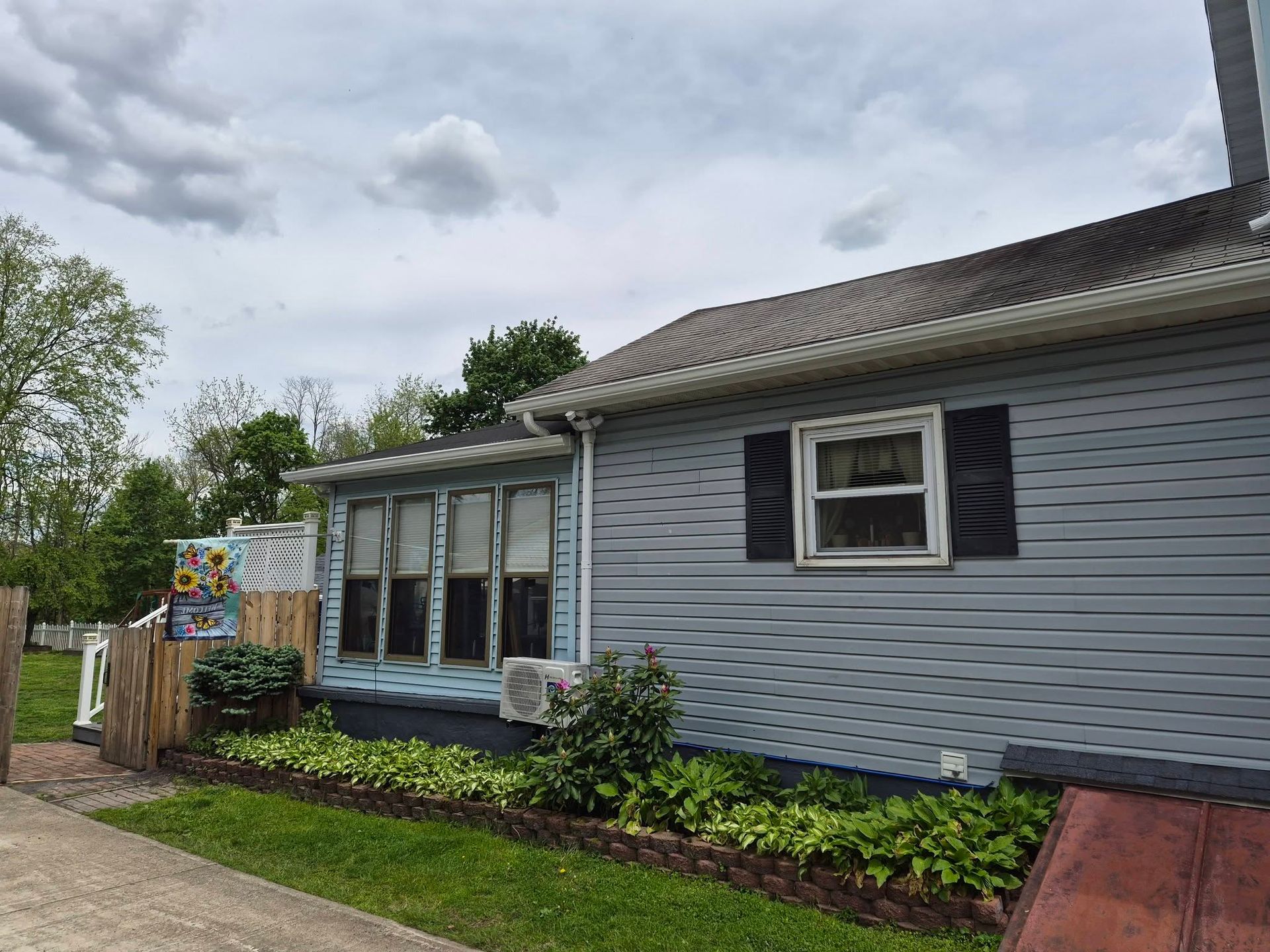 Suburban house with gray siding, black shutters, flower beds, and a cloudy sky