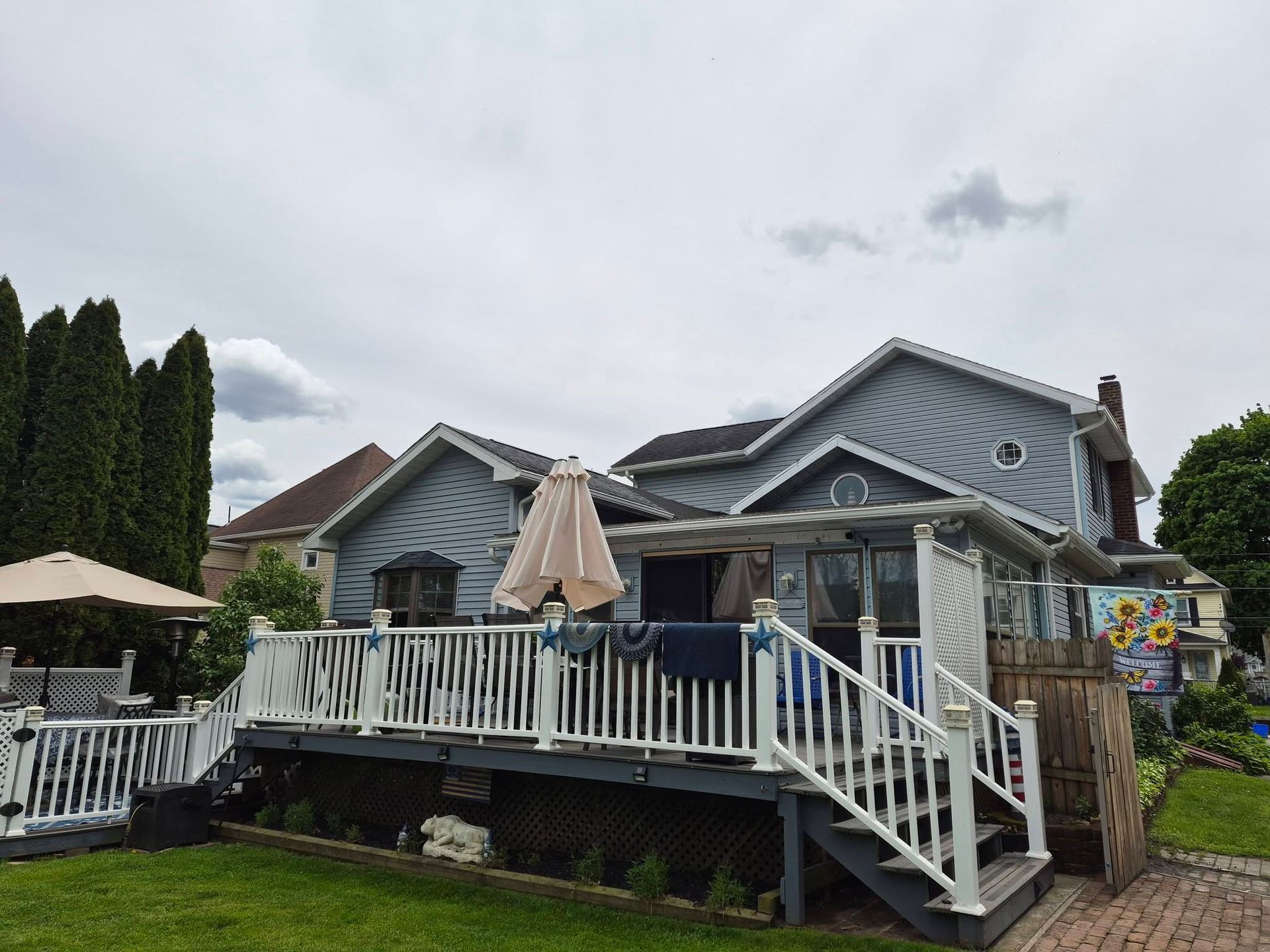 Backyard deck with white railing, patio umbrellas, and a blue-gray house under a cloudy sky