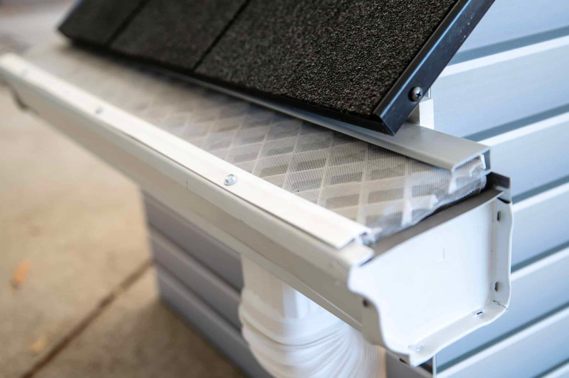 Close-up of a metal roof gutter with a leaf guard and dark shingles above it