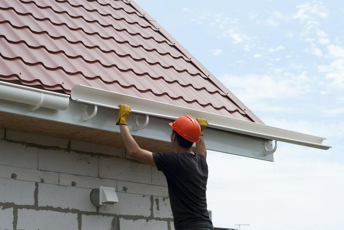 Worker in orange hard hat cleaning a roof gutter on a house