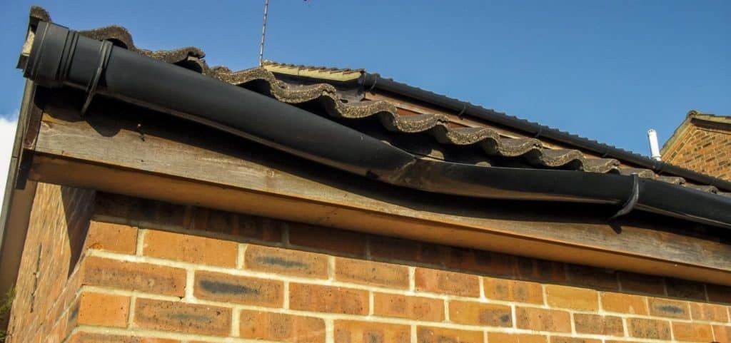 Close-up of a brick house roof with black guttering and corrugated roofing under a blue sky