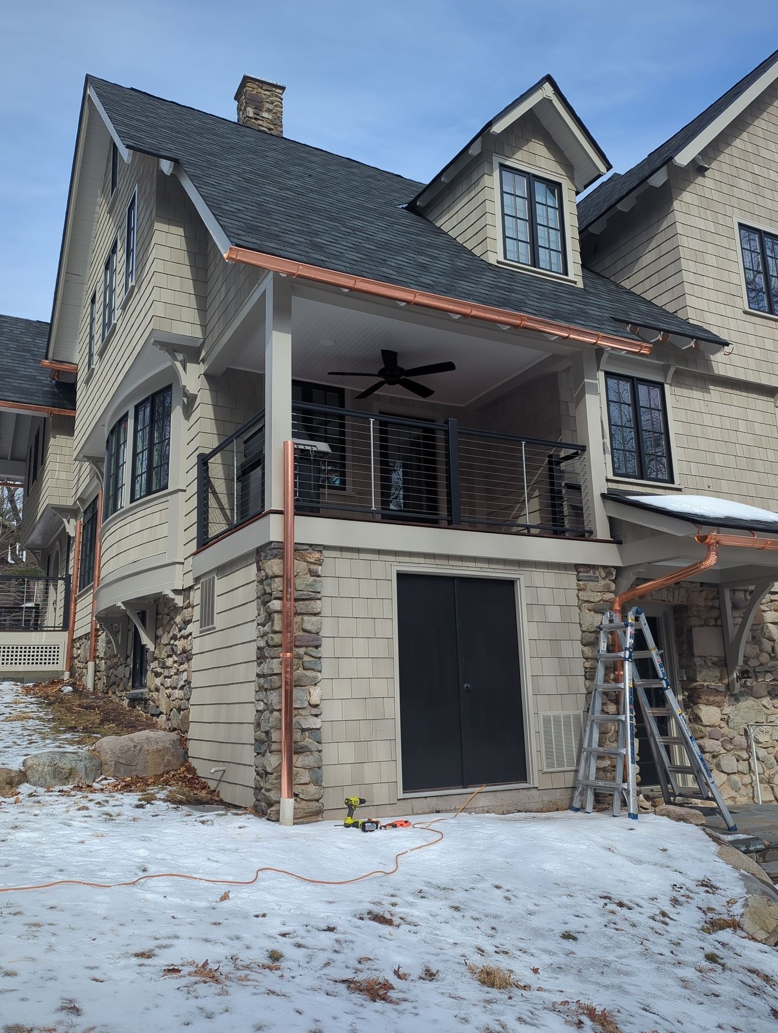 Snow-covered stone house under construction with a covered porch and ladder outside