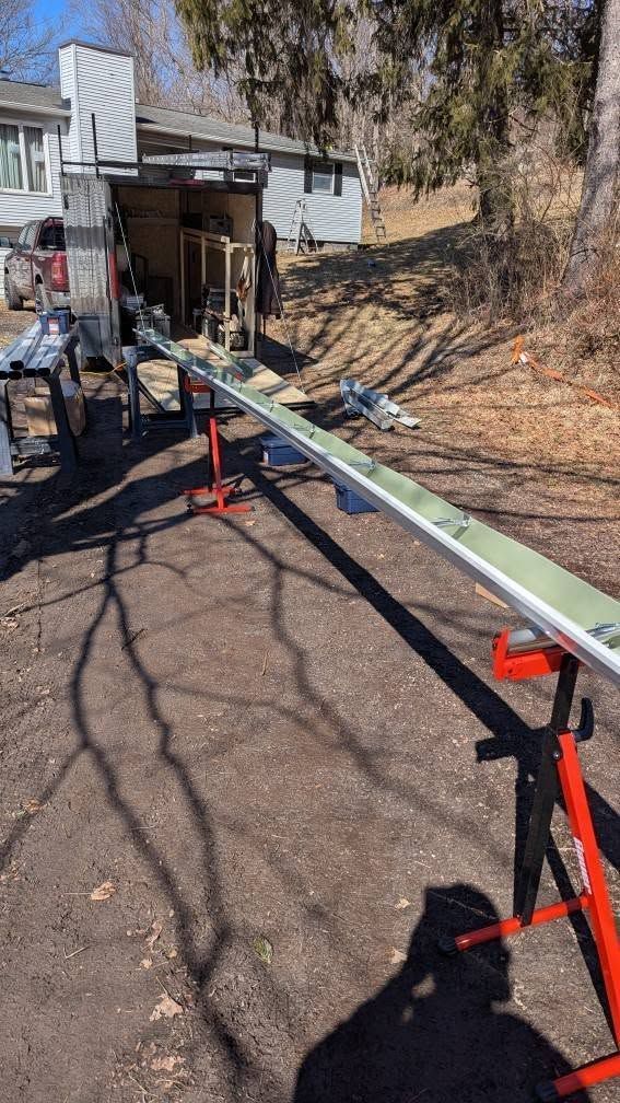 A long green beam balanced on red saw horses outside a house, with tools and trees in the yard.