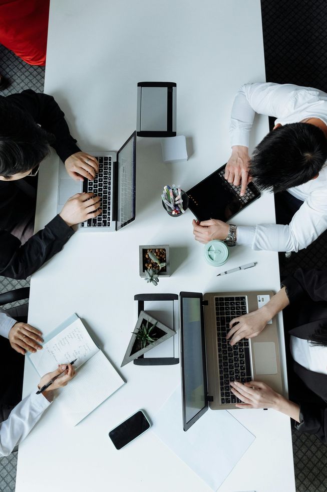 Overhead view of four people collaborating around a table with laptops, tablets, notebooks, and coffee.