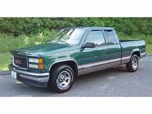 A green gmc truck is parked on the side of the road.