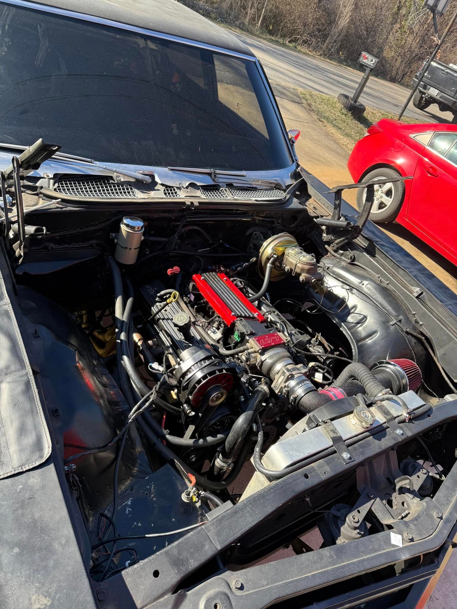 A black car with the hood open and a red car in the background.