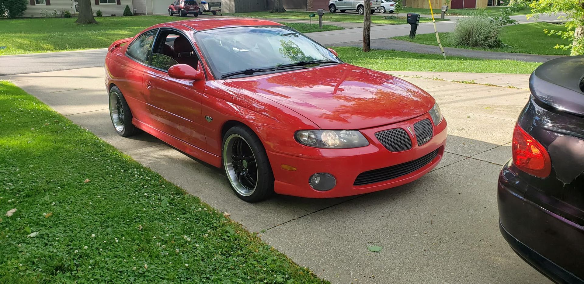 A red car is parked in a driveway next to a black car.
