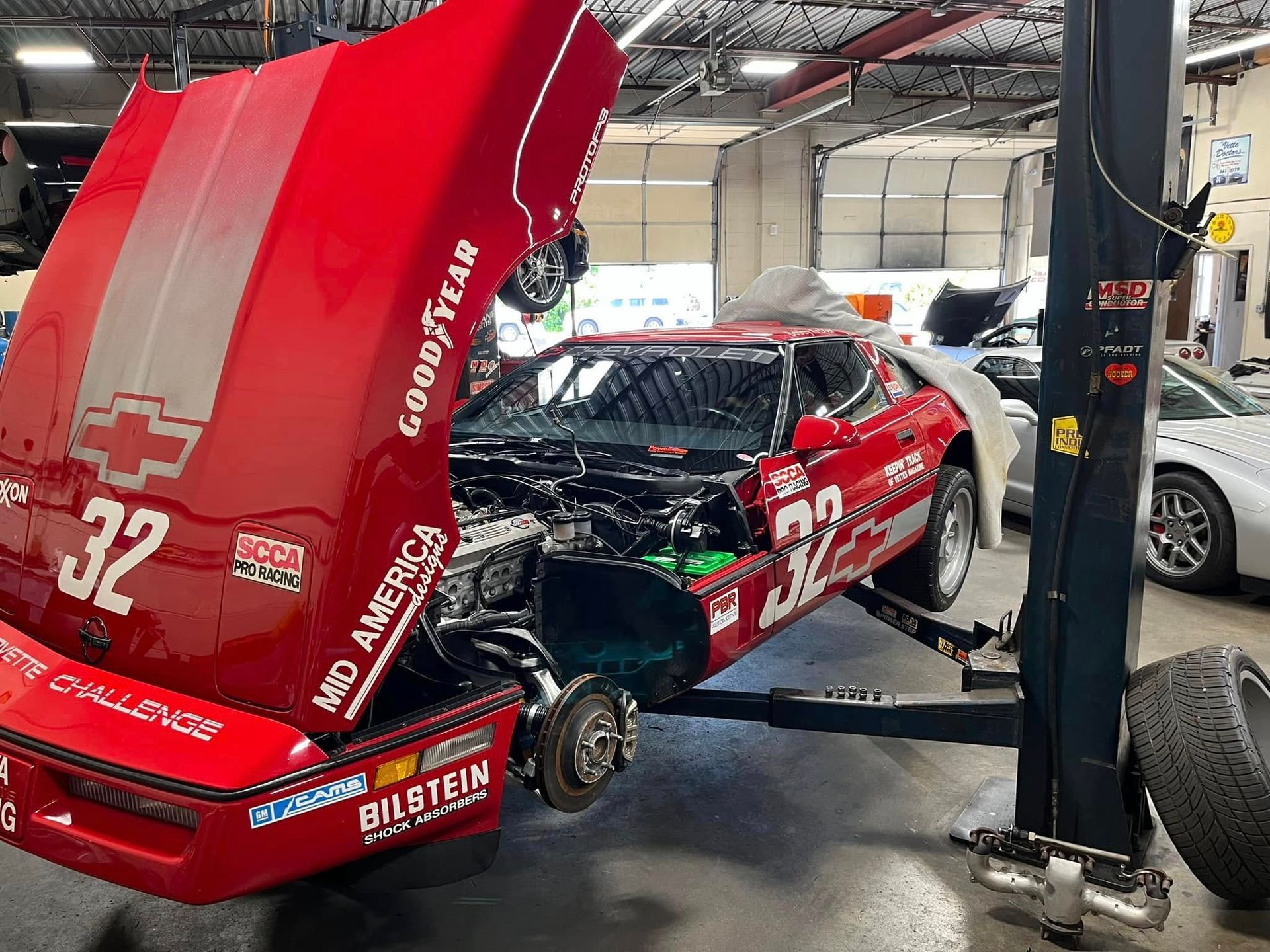 A red race car with the hood open is on a lift in a garage.