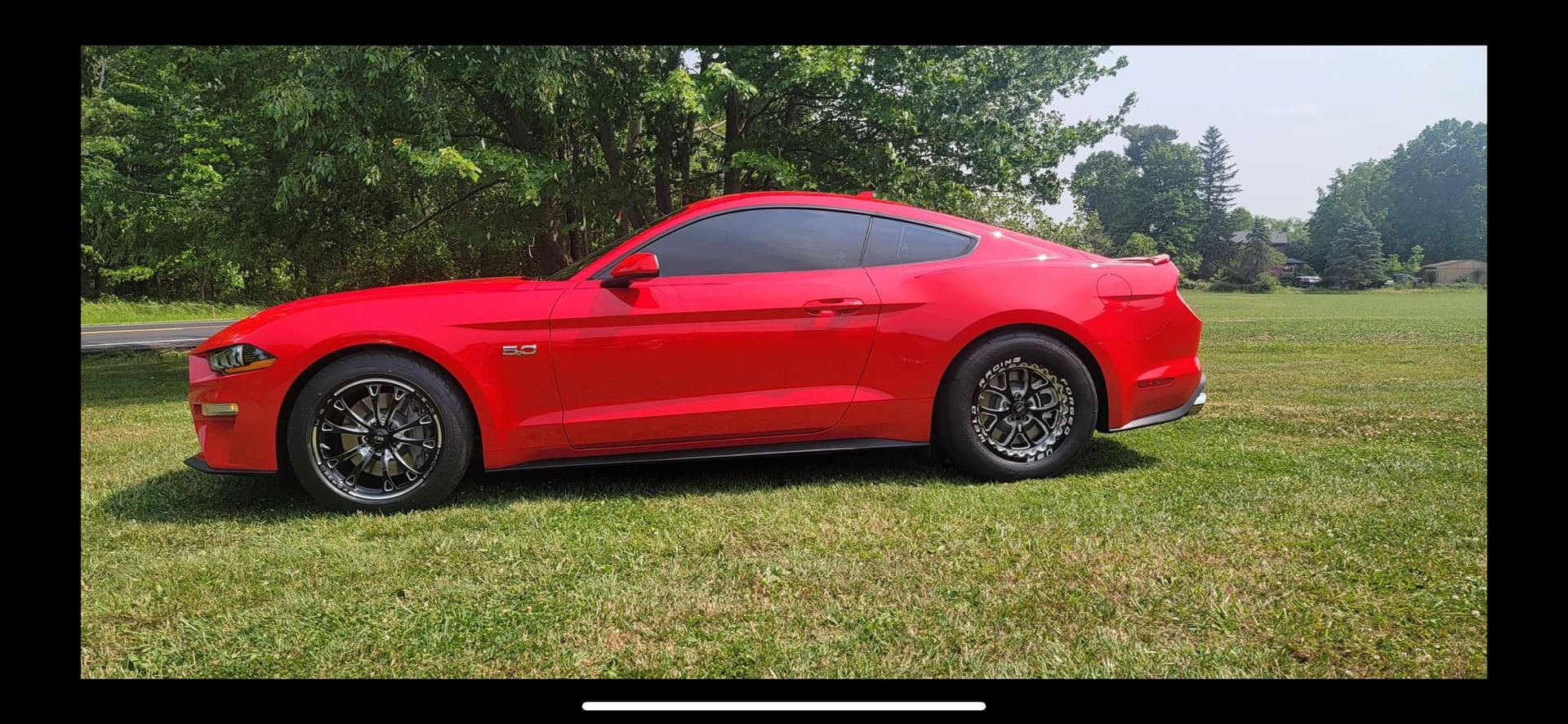 A red mustang is parked in a grassy field.