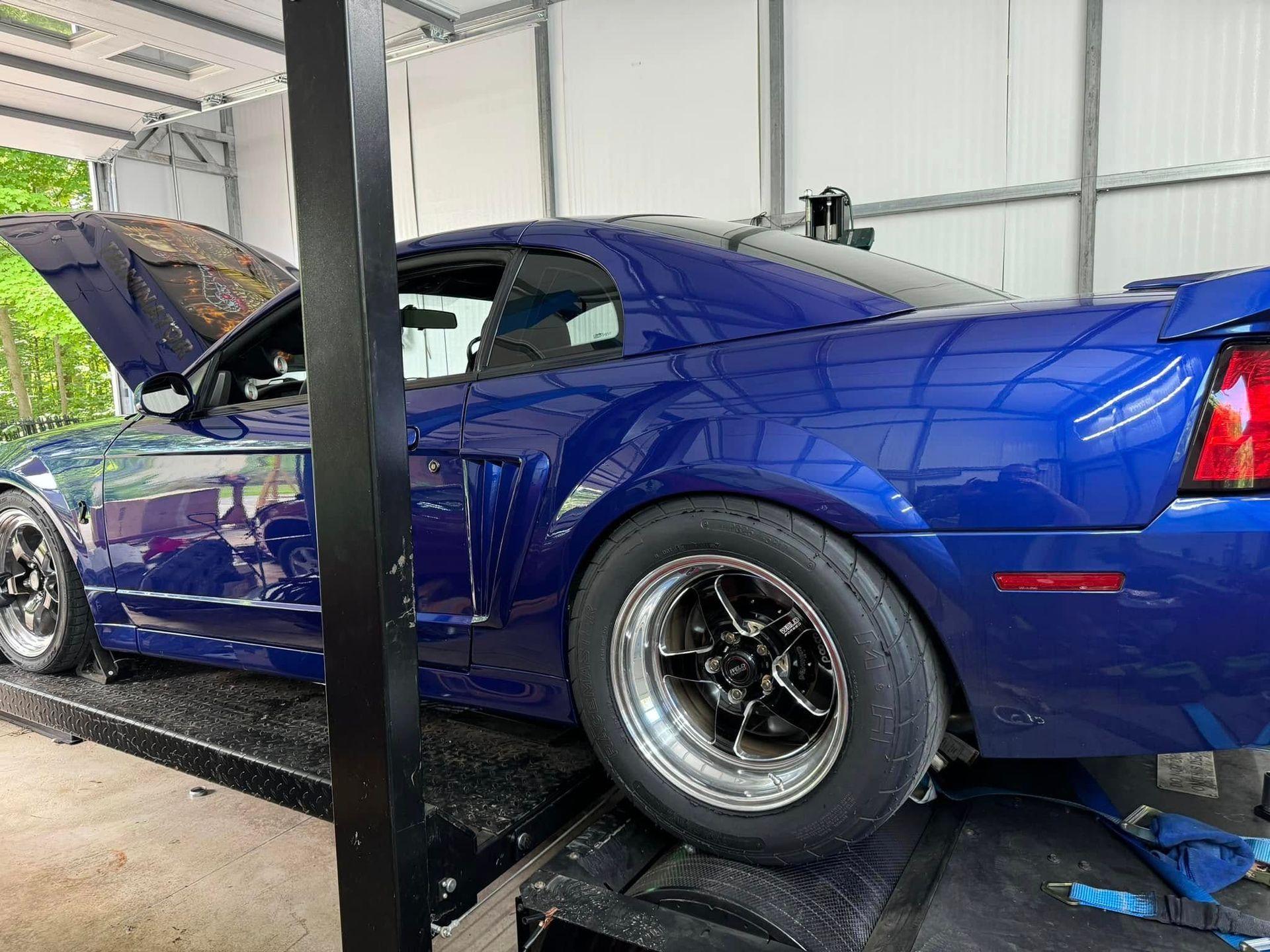 A blue mustang is parked in a garage with the hood up.