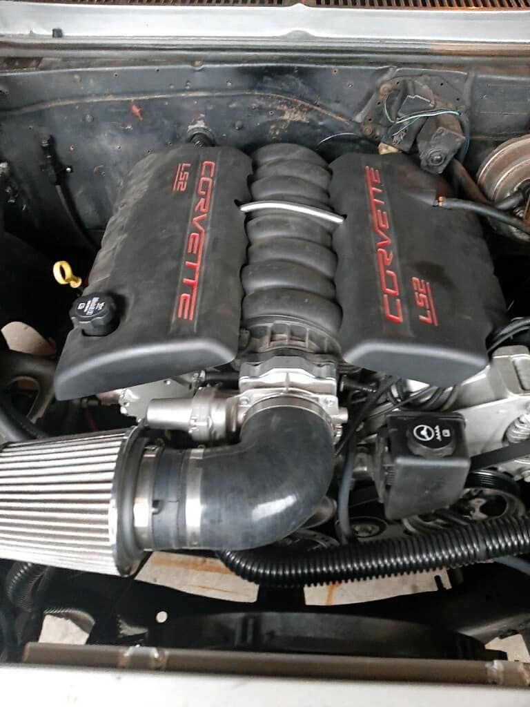 A corvette engine is sitting under the hood of a car.