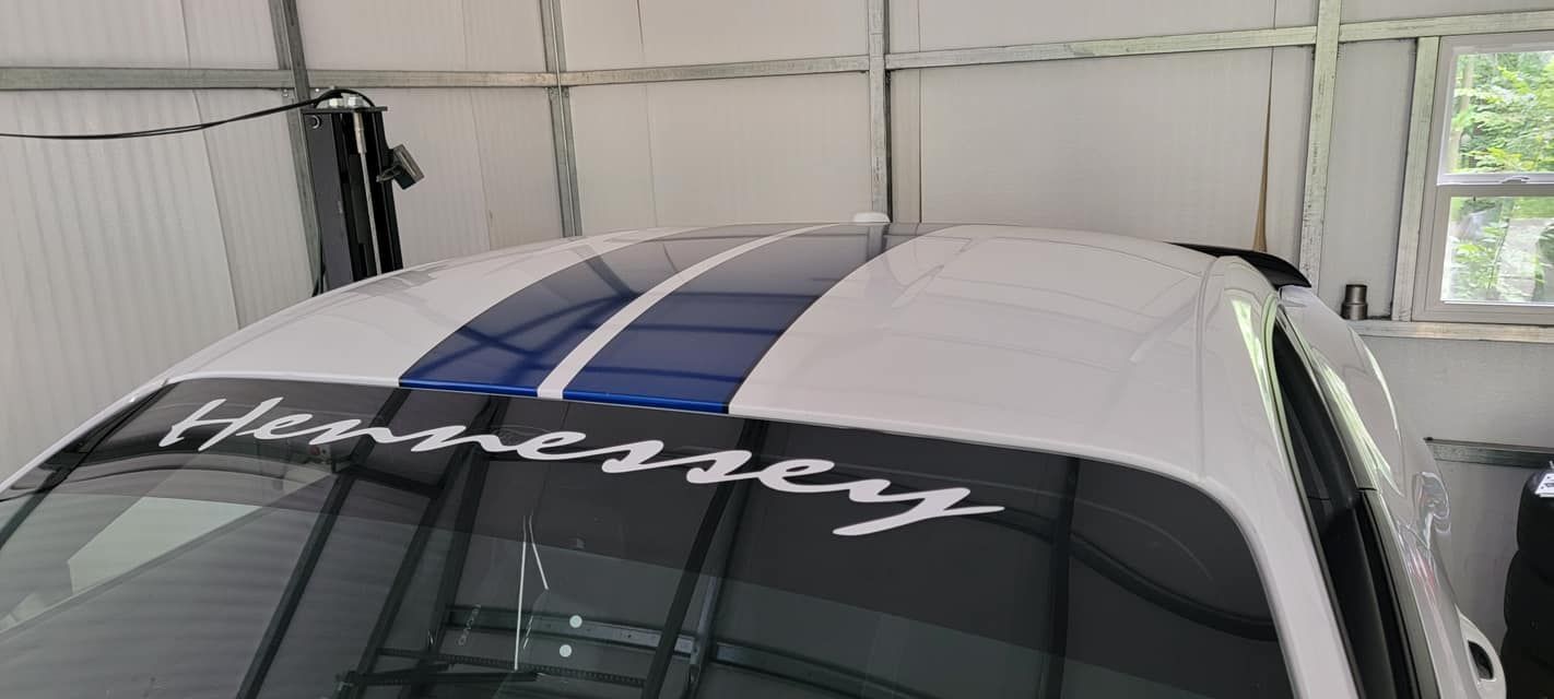 A white car with blue stripes on the roof is parked in a garage.