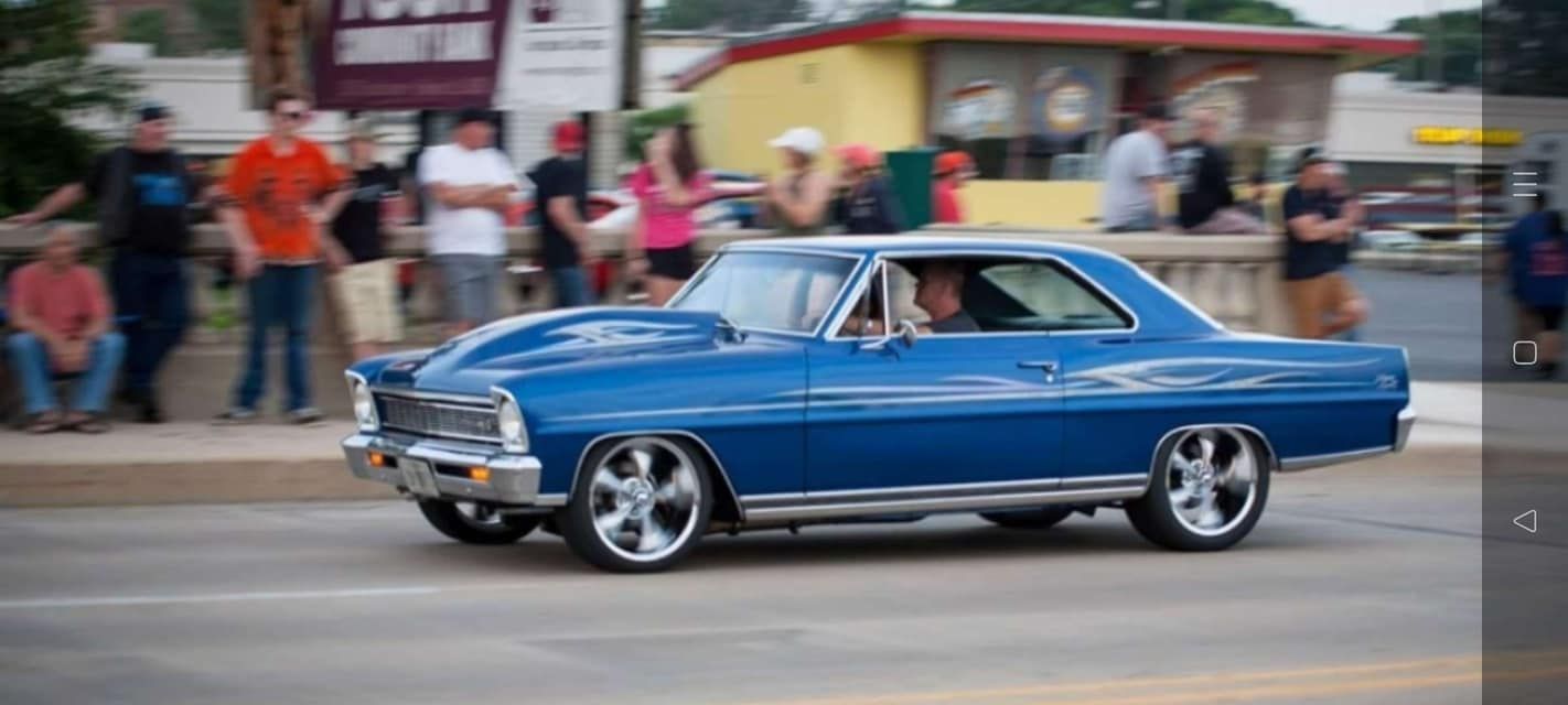 A blue car is driving down a street with people watching.