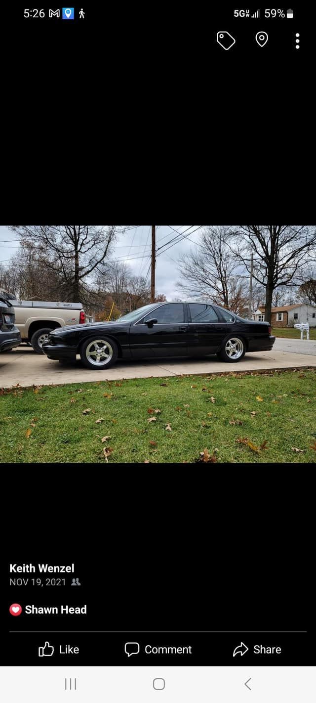 A black car is parked in a driveway next to a grassy field.