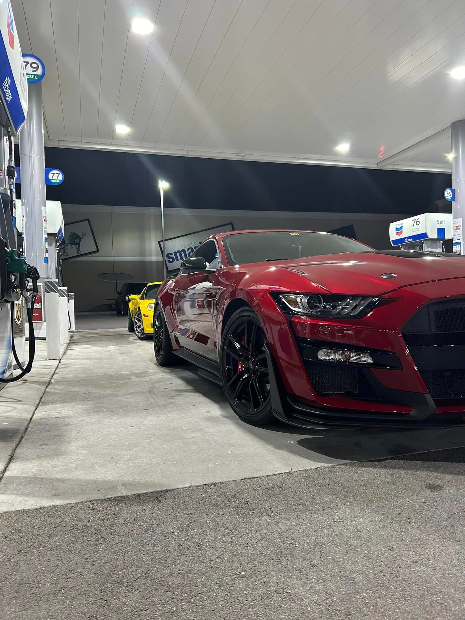 A red mustang is parked at a gas station at night.