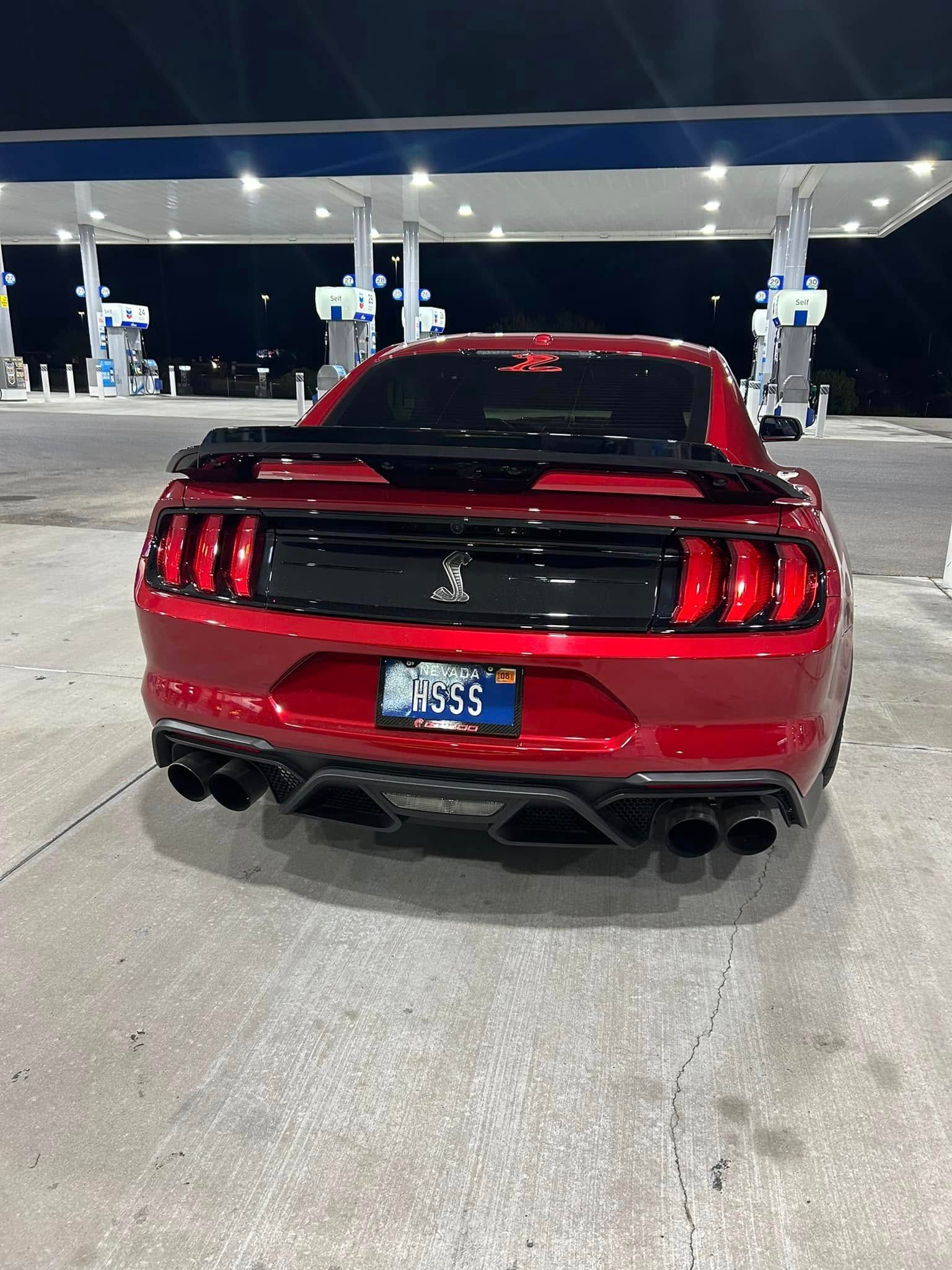 A red mustang is parked in a gas station at night.
