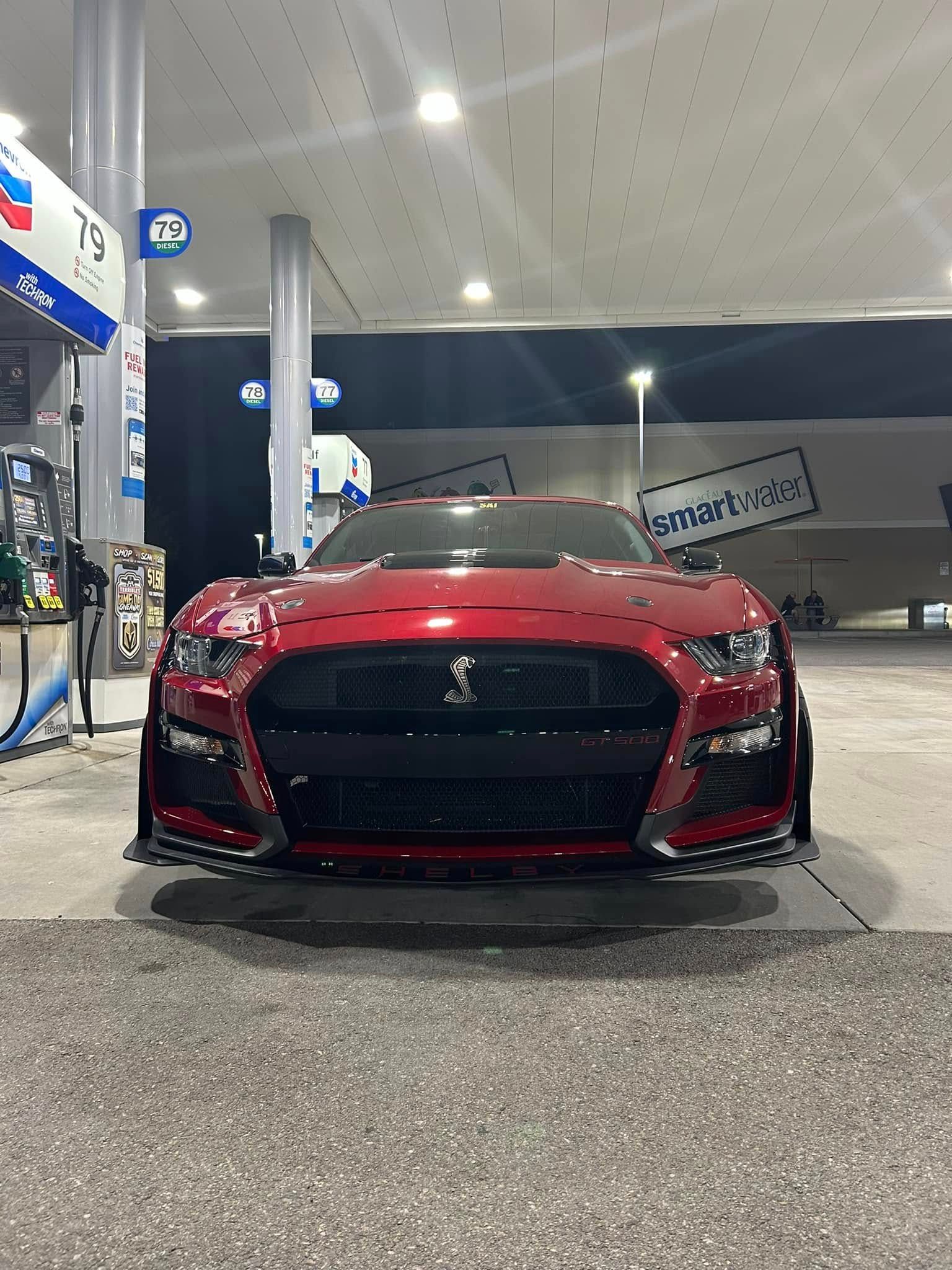 A red mustang is parked at a gas station at night.