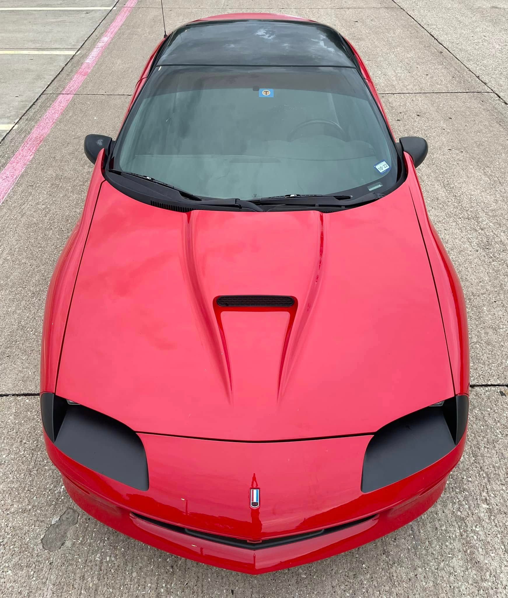 A red car with a black hood is parked in a parking lot.