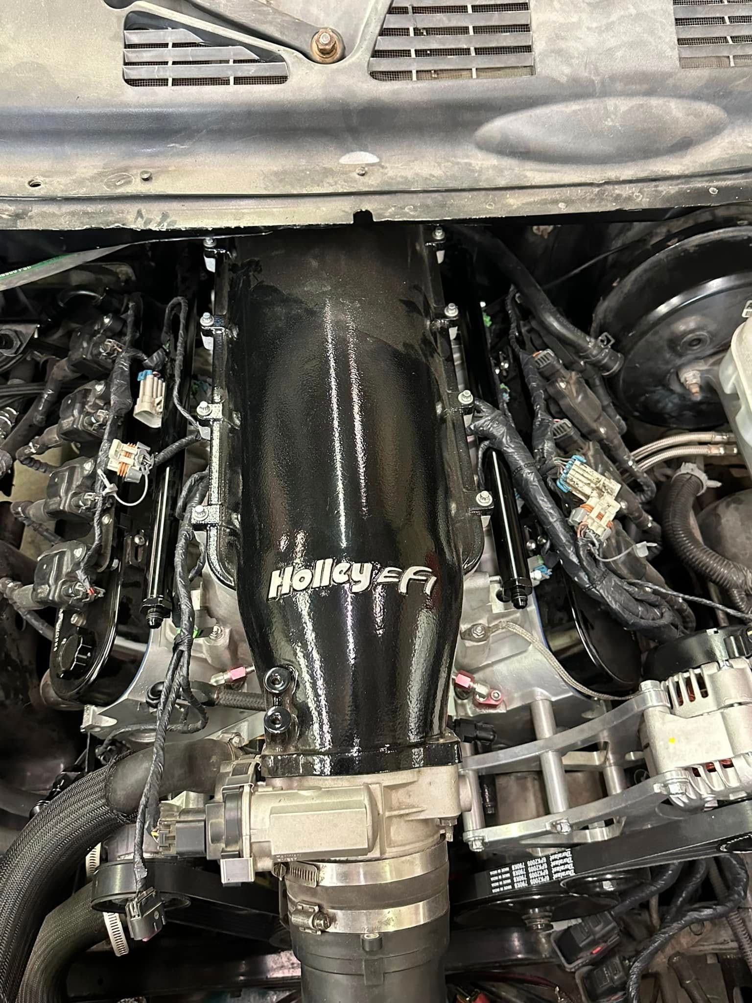 A close up of a car engine with a hose attached to it.