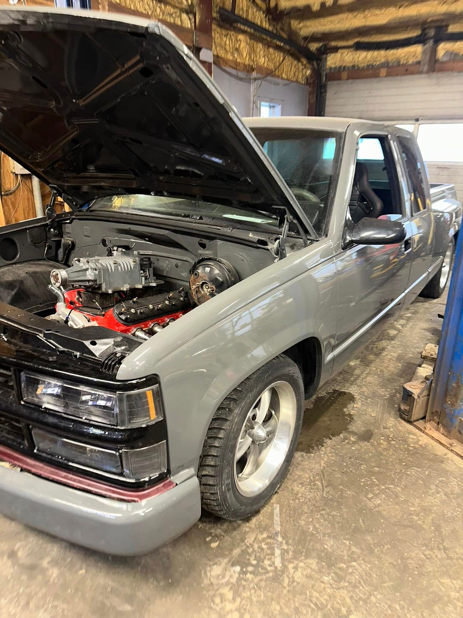 A gray truck with the hood up is parked in a garage.