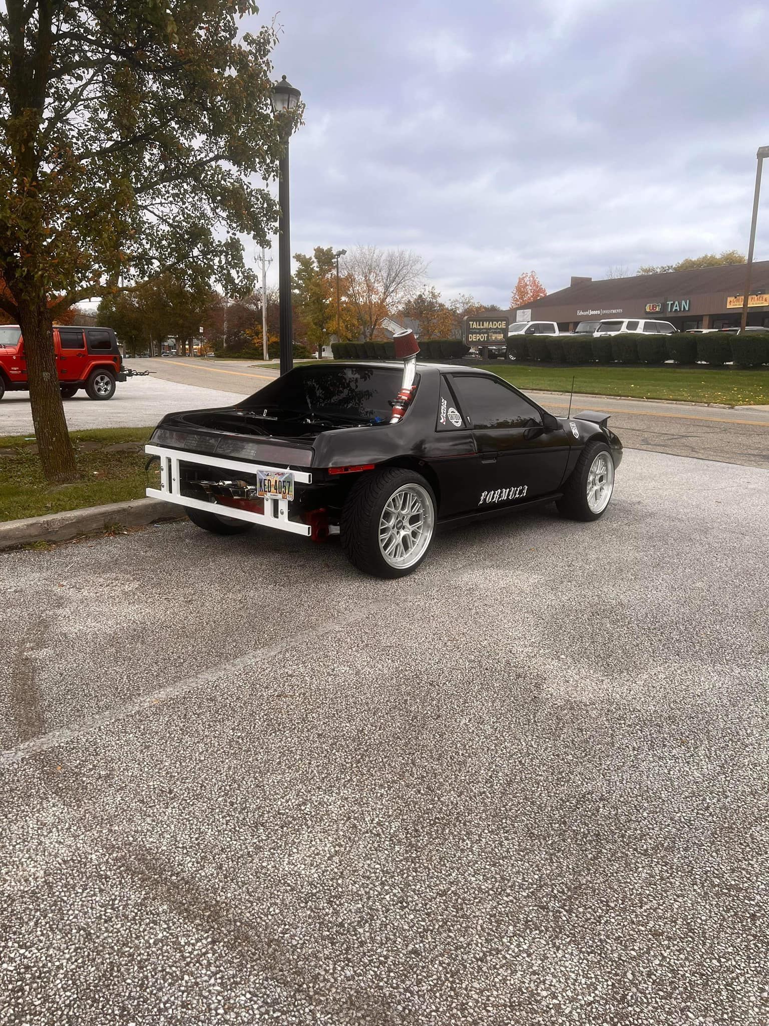 A black car is parked in a gravel lot.