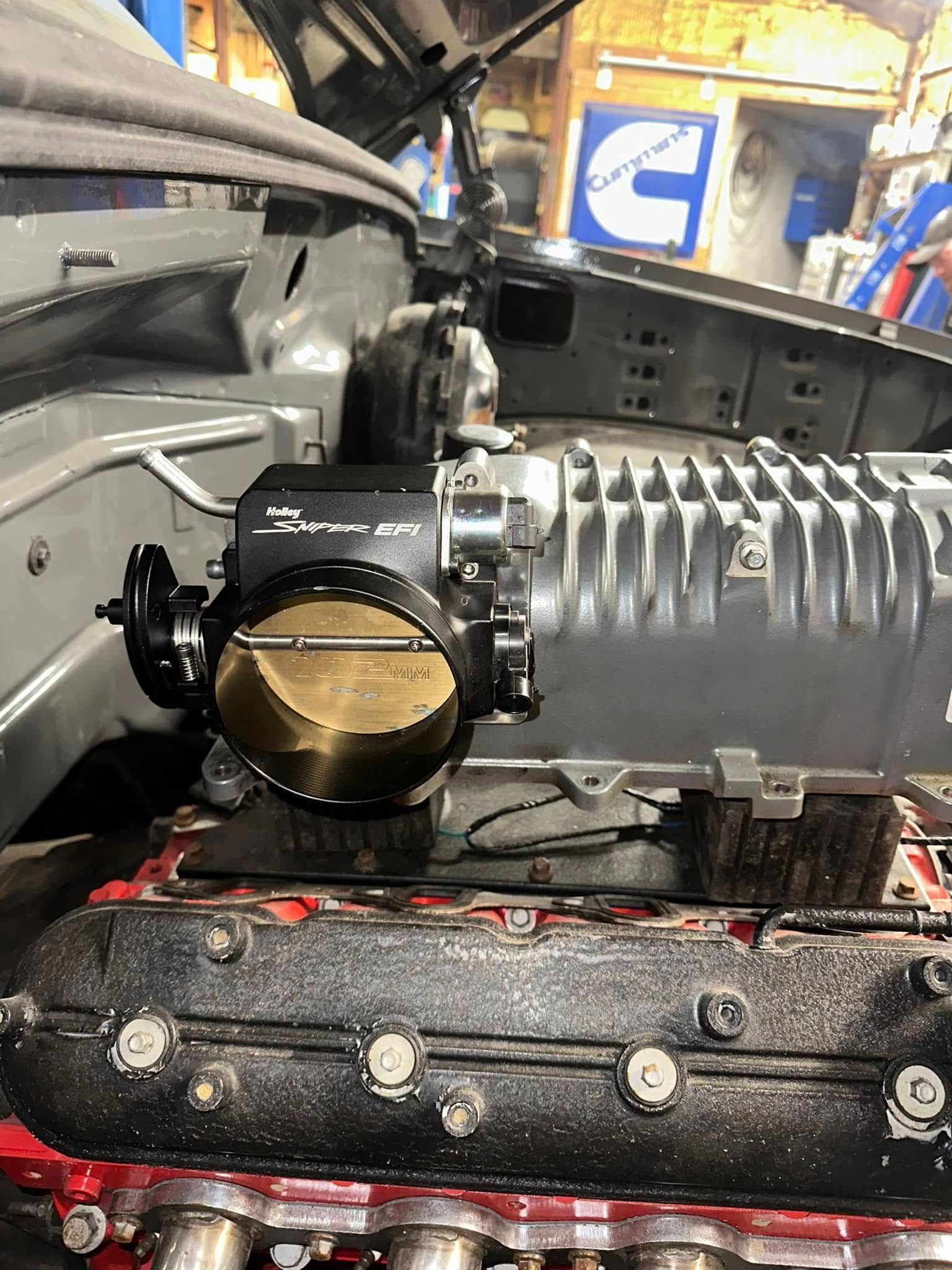 A close up of a car engine with the hood open in a garage.
