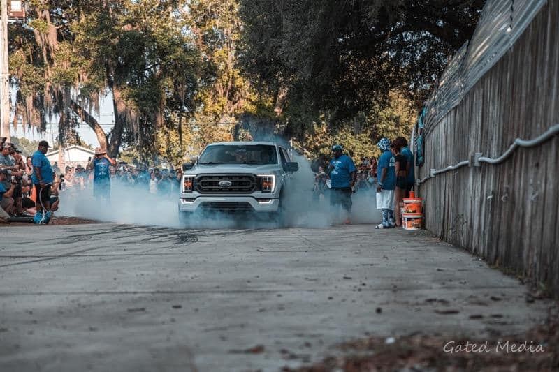 A white truck is driving down a street with smoke coming out of it.