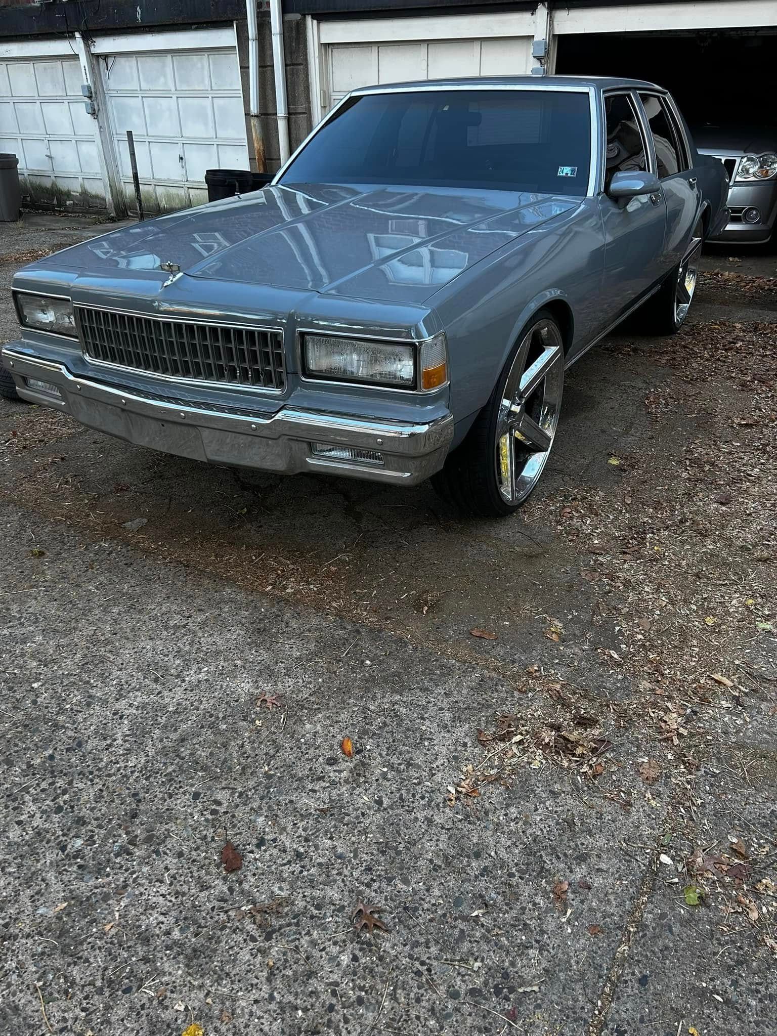 A silver car is parked in a gravel lot in front of a garage.