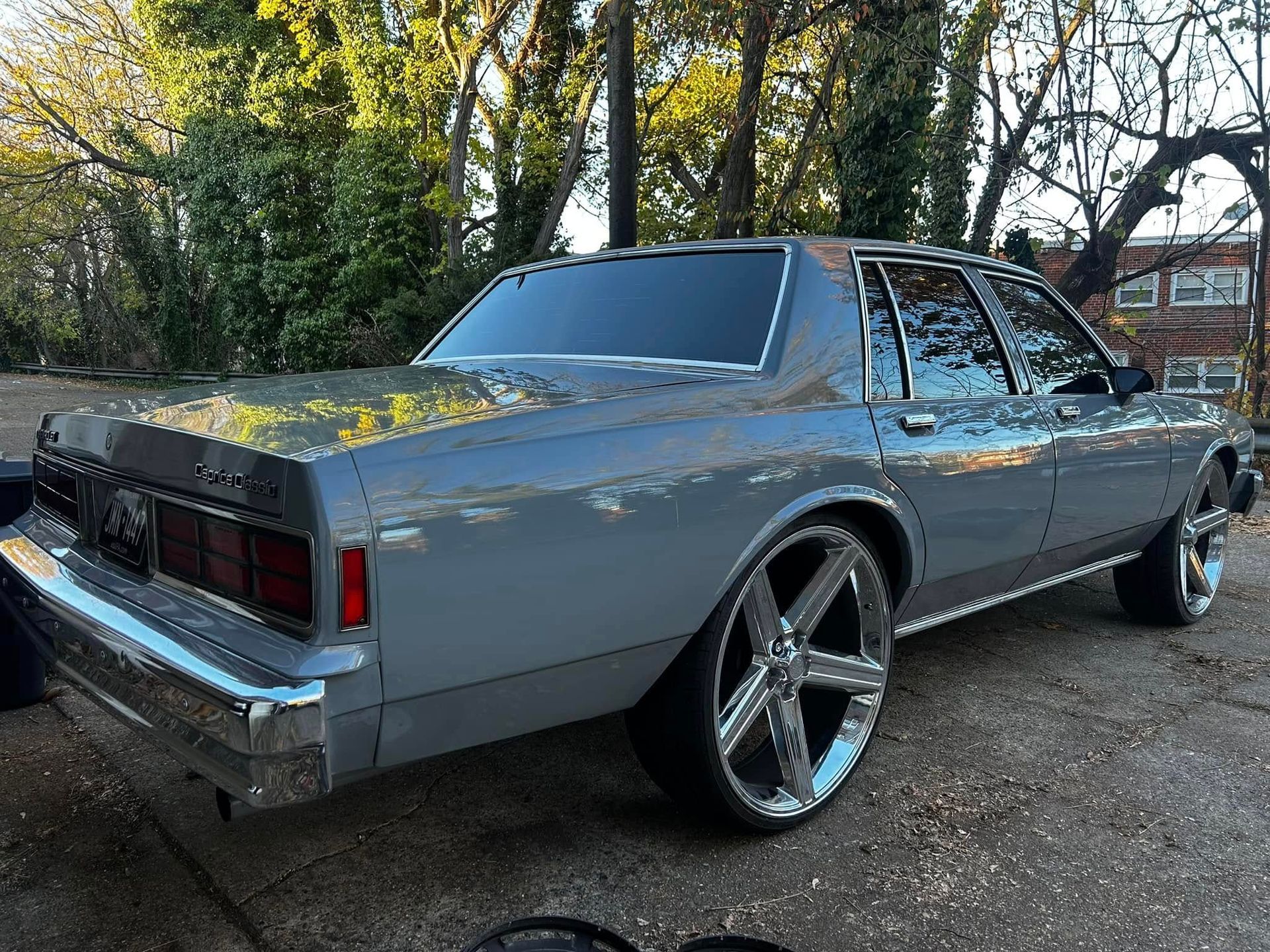 A silver car is parked in a driveway with trees in the background
