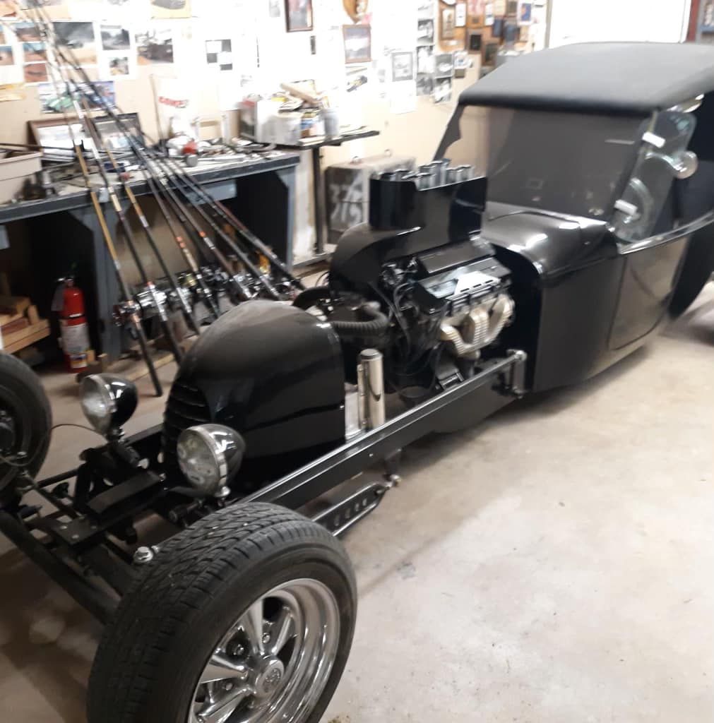 A black car is parked in a garage next to fishing rods.