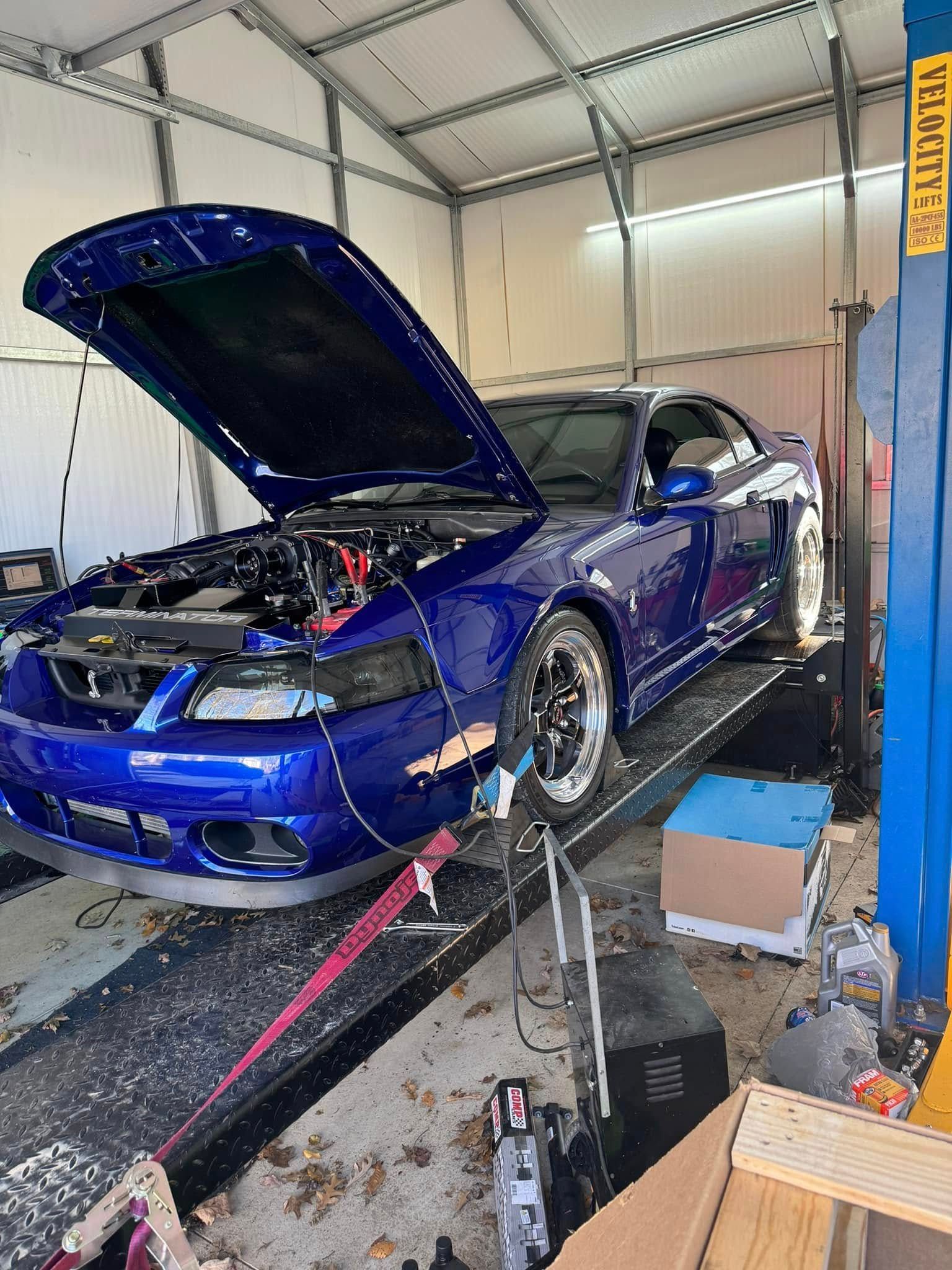 A blue mustang is sitting on a lift in a garage with its hood open.