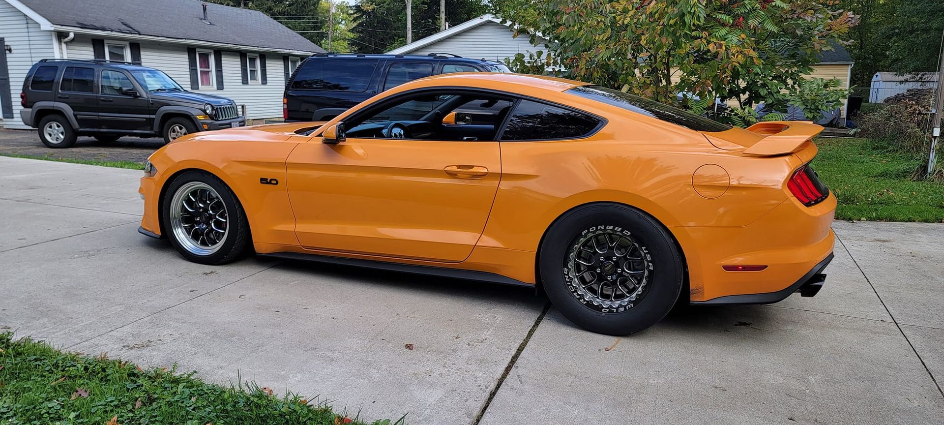 A yellow mustang is parked on the side of the road in front of a house.