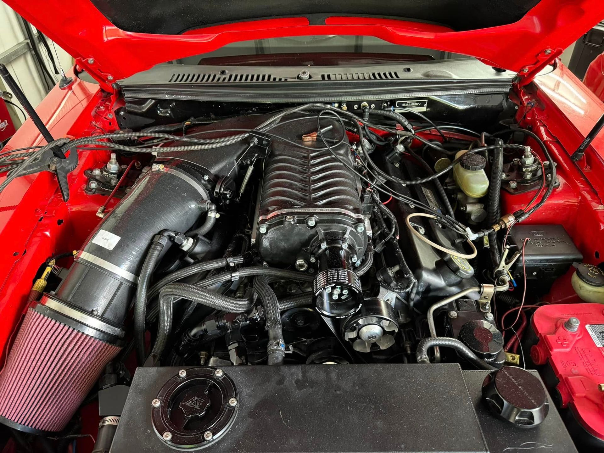 The engine of a red mustang with the hood up