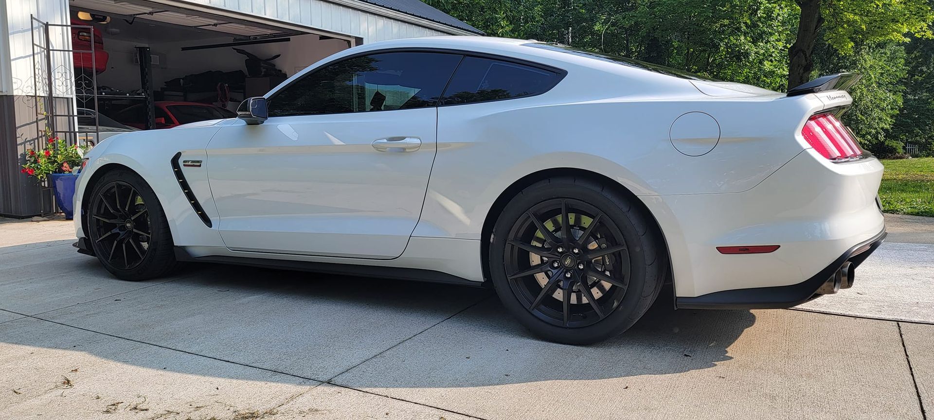 A white ford mustang is parked in a driveway in front of a garage.