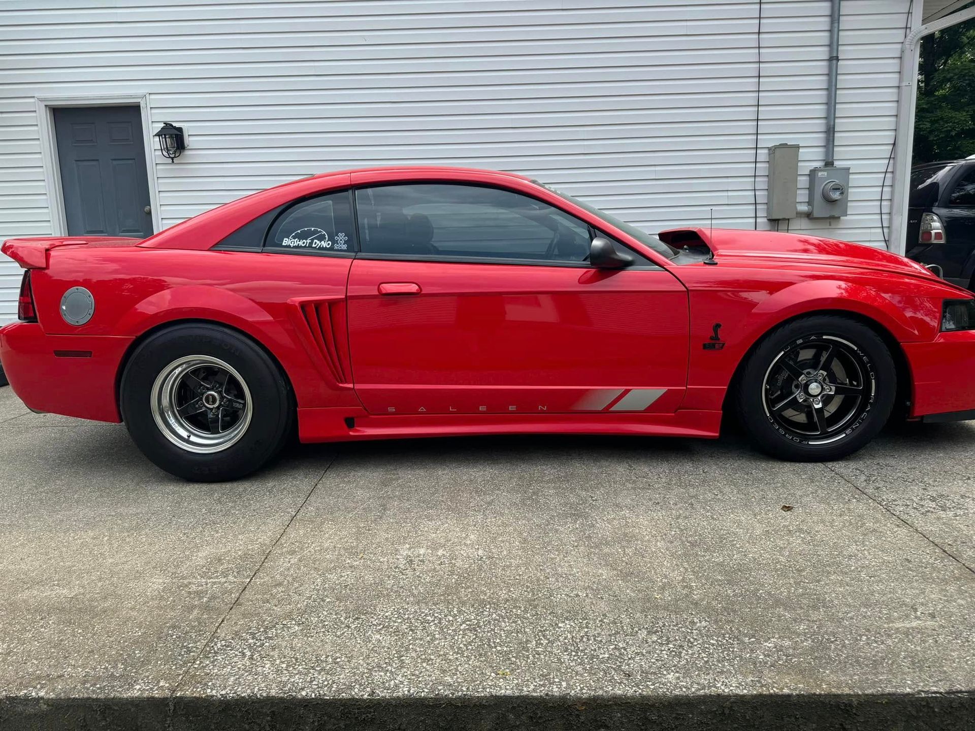 A red mustang is parked in front of a white building.