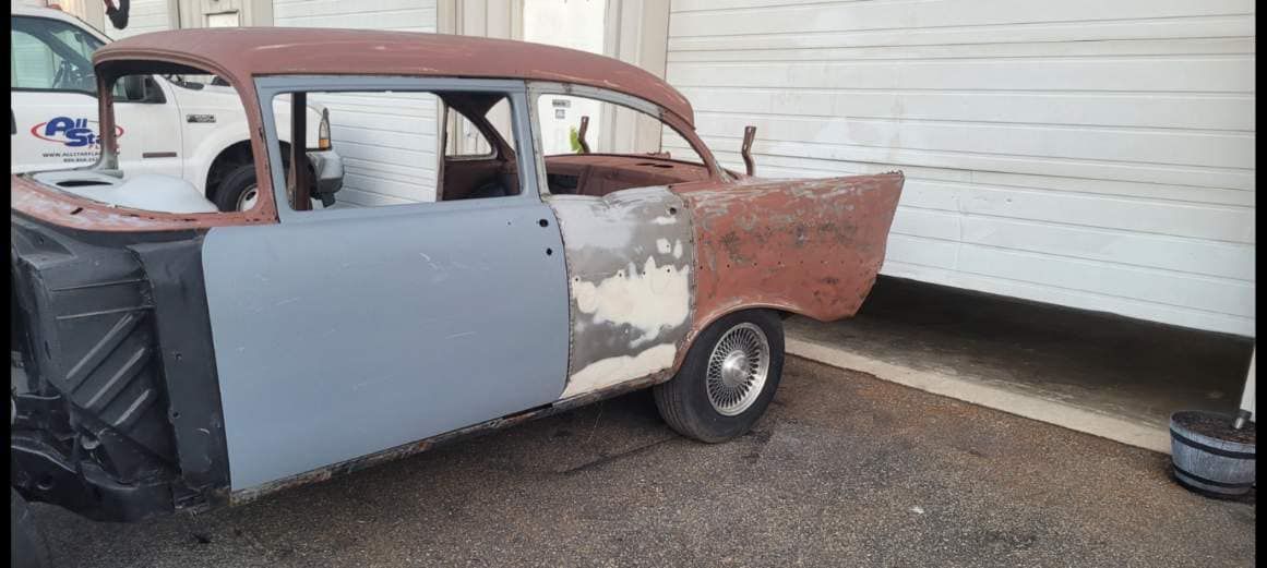 An old rusty car is parked in front of a garage door.