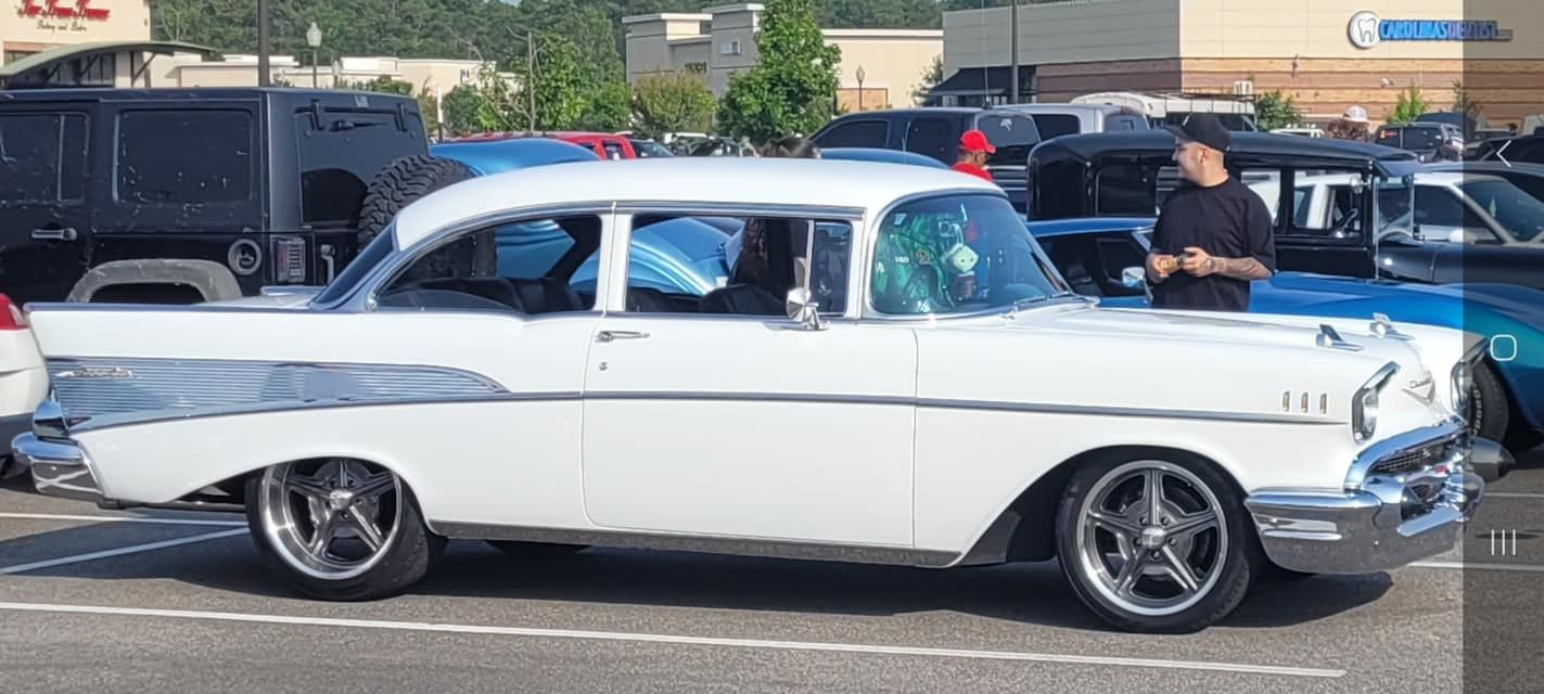 A man is standing next to a white car in a parking lot.