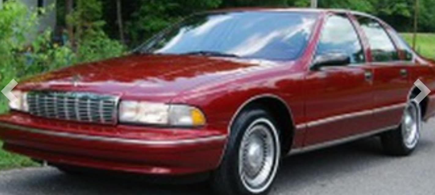 A red car with white tires is parked on the side of the road.