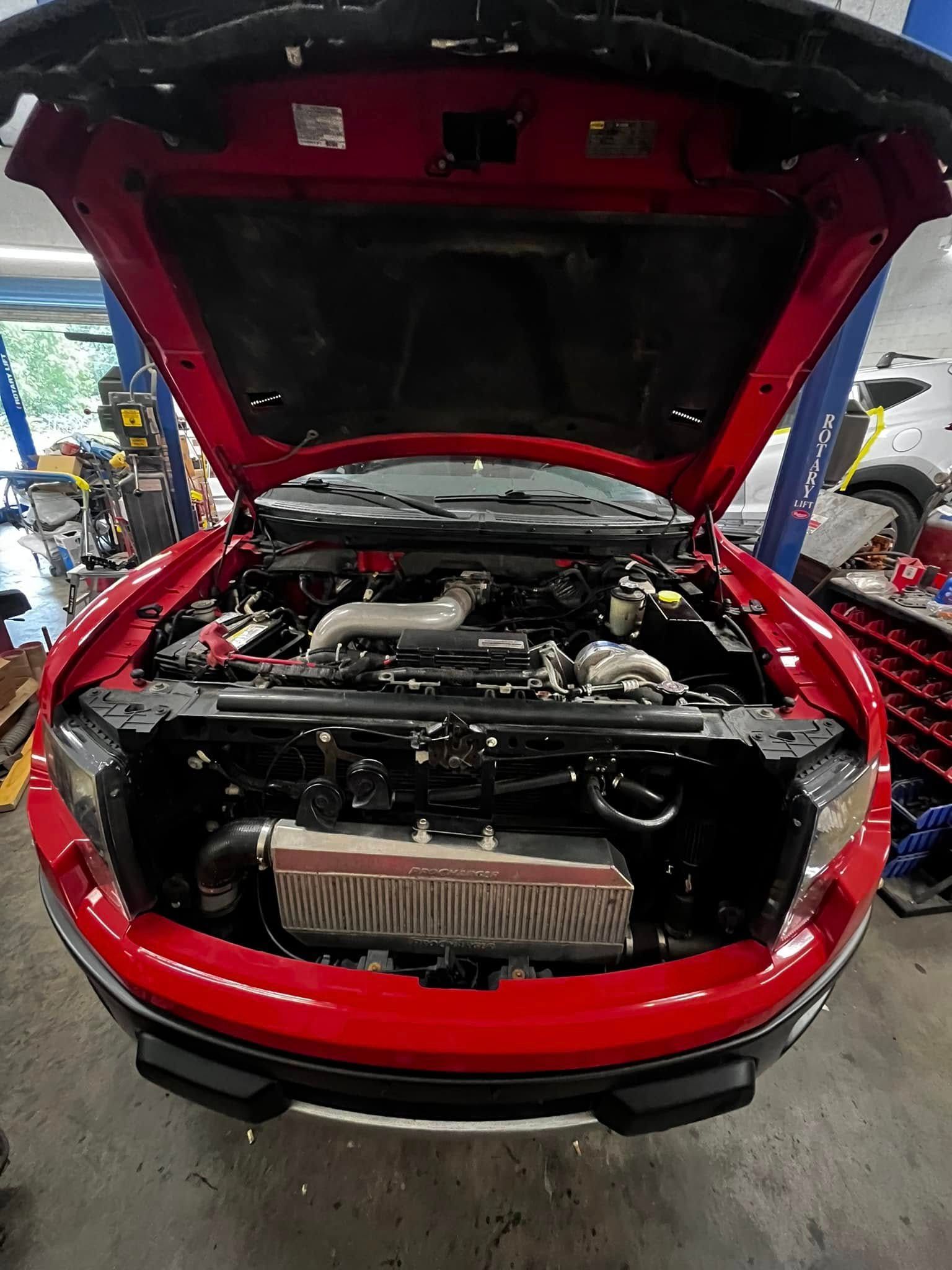 A red car with the hood up in a garage.