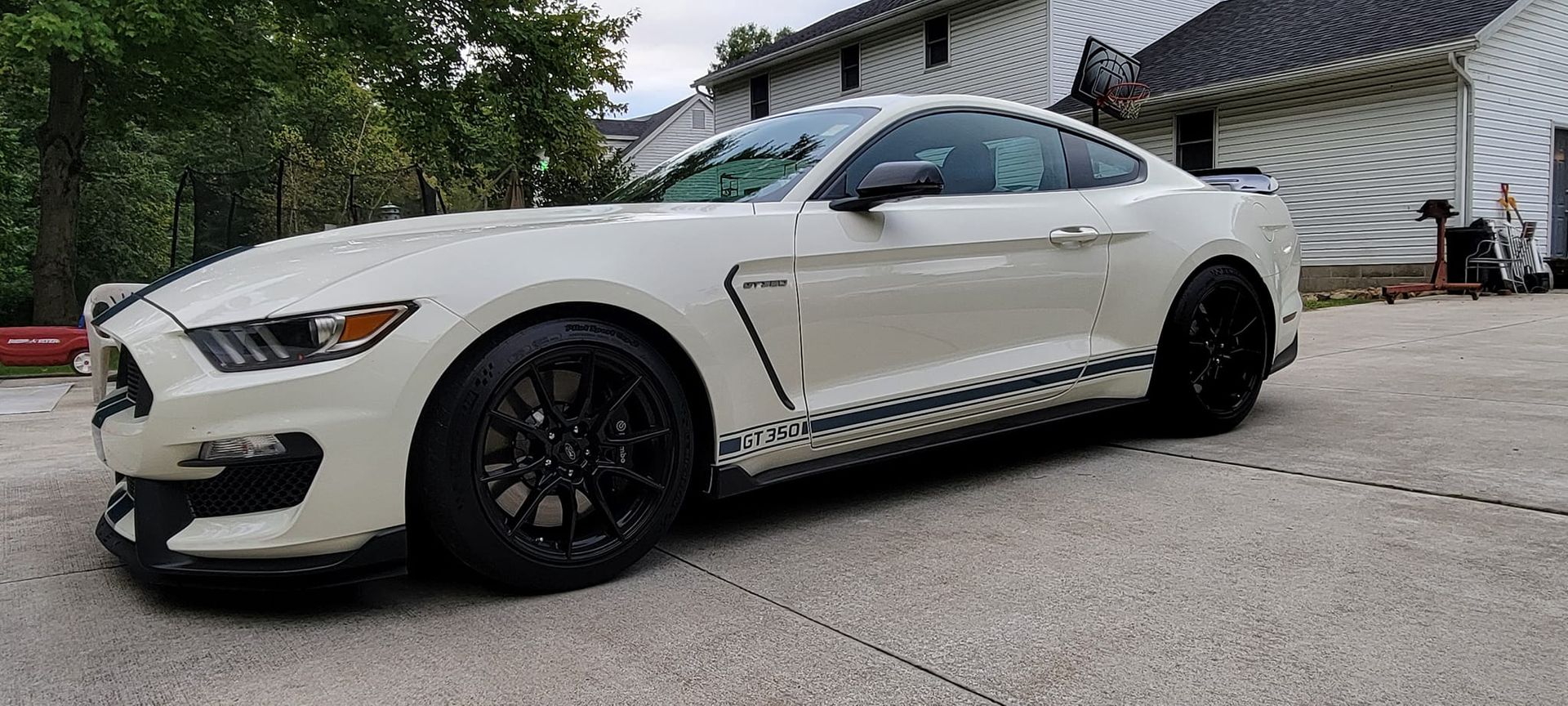 A white ford mustang is parked in a driveway in front of a house.