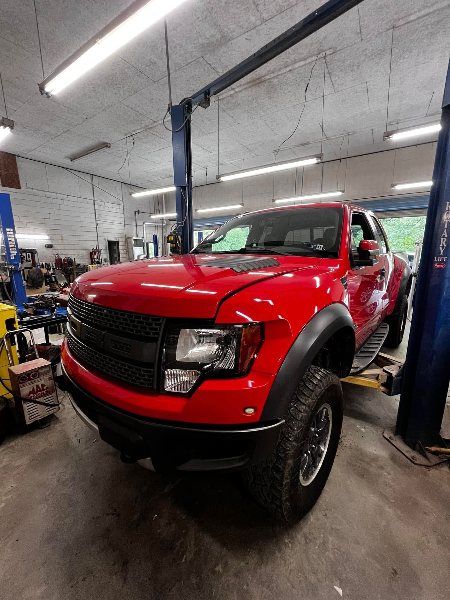 A red truck is sitting on a lift in a garage.