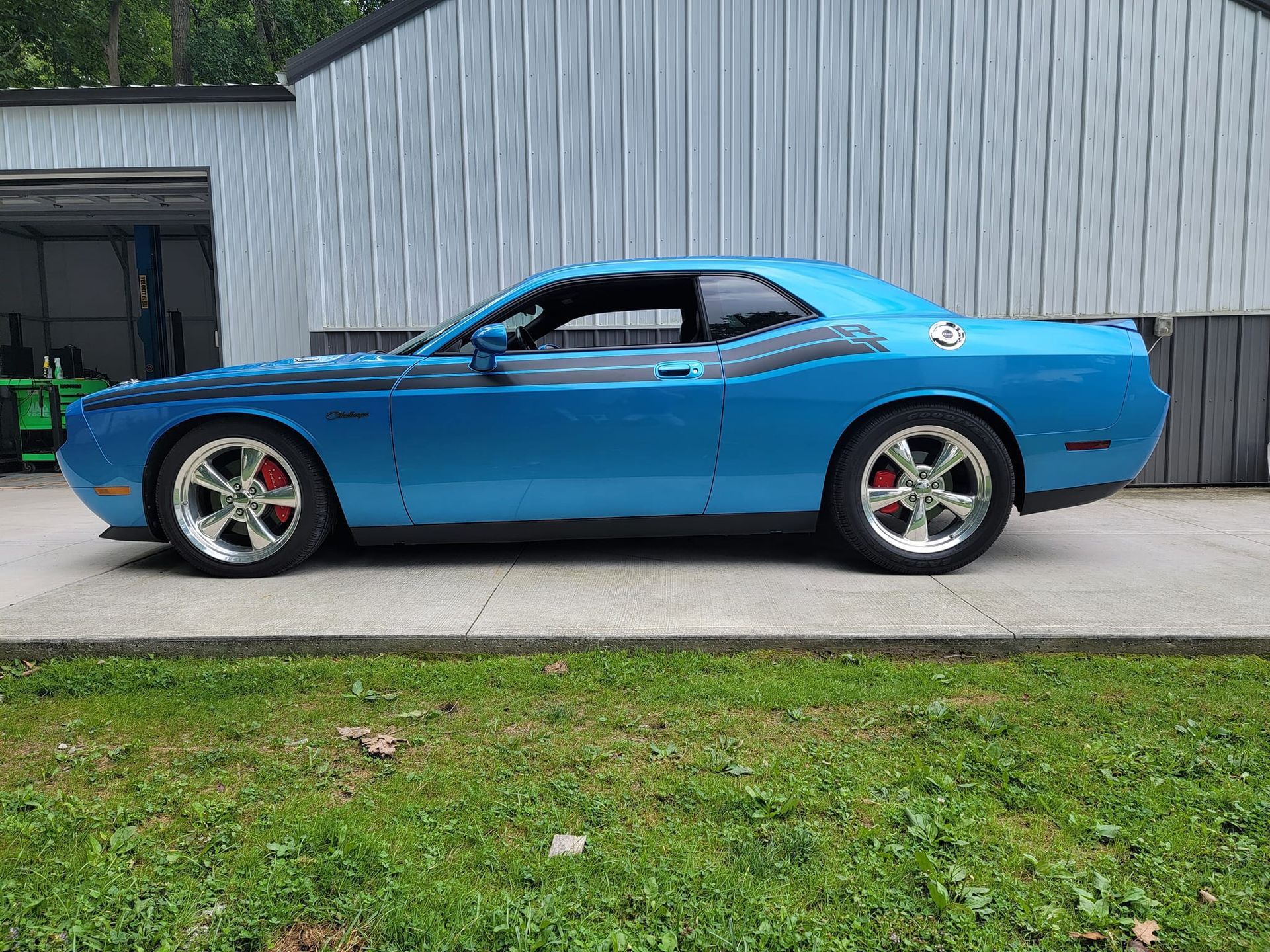 A blue dodge challenger is parked in front of a garage.