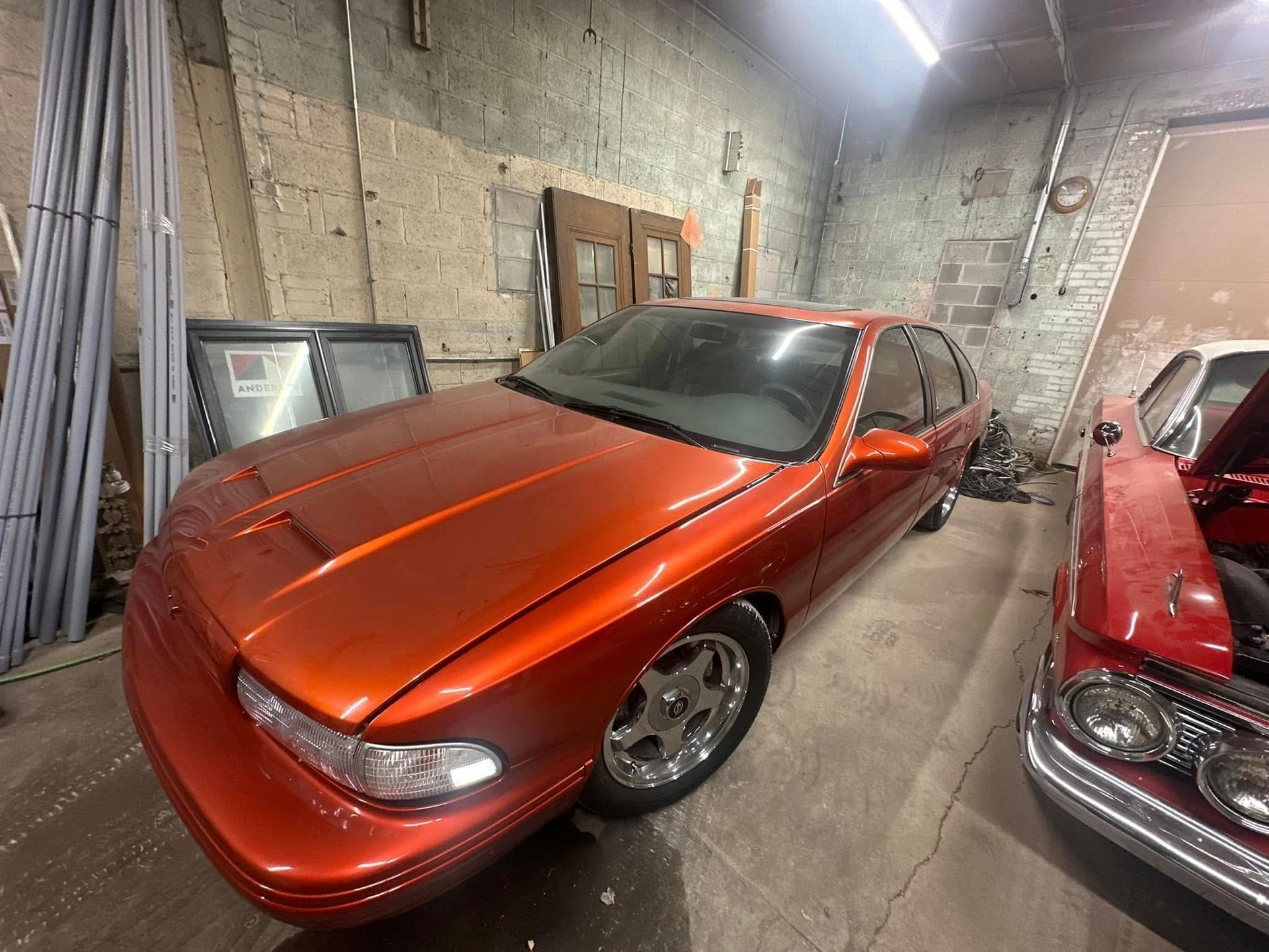 A red car is parked in a garage next to a white car.