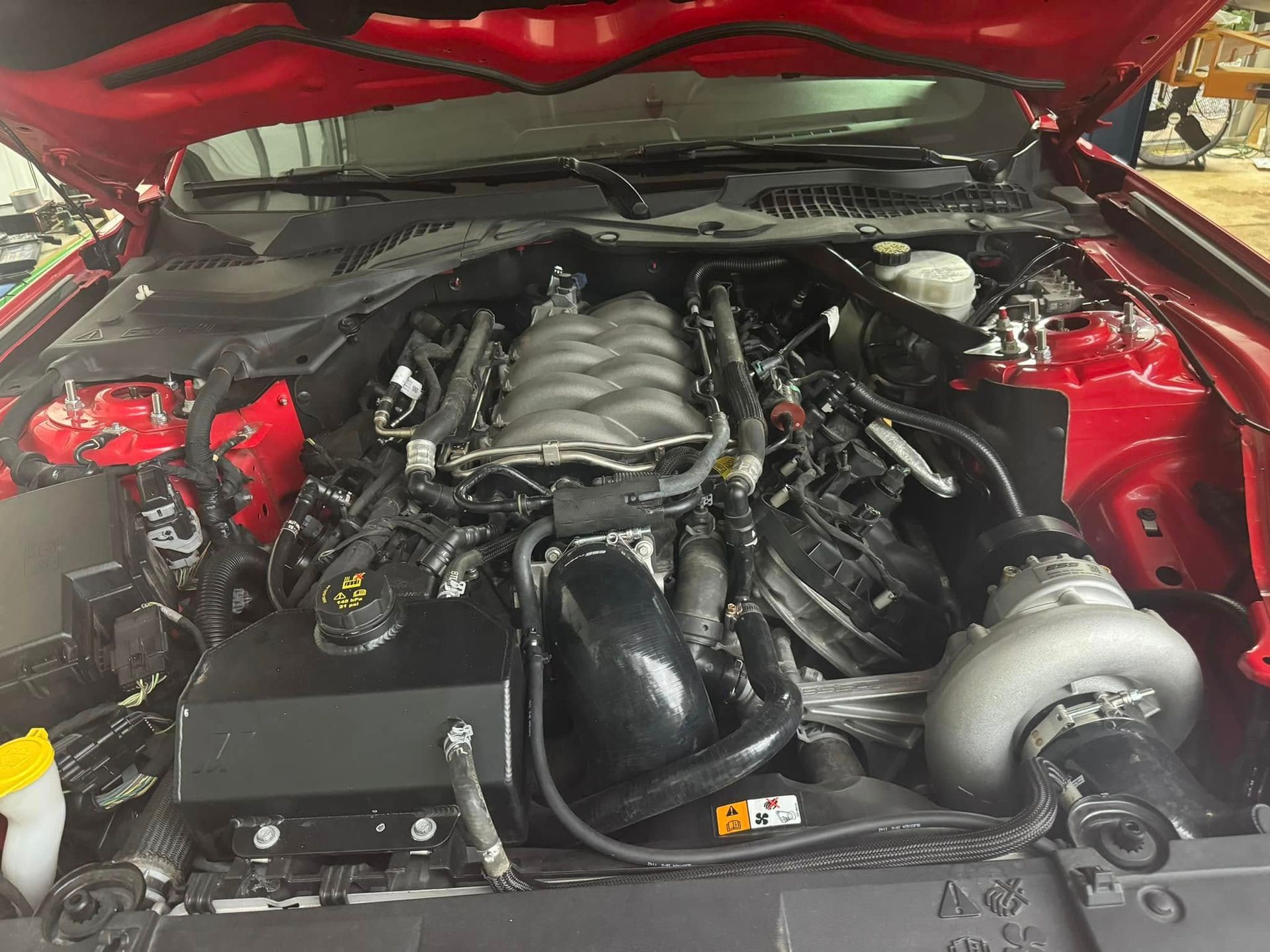 The engine of a red mustang is shown with the hood open.