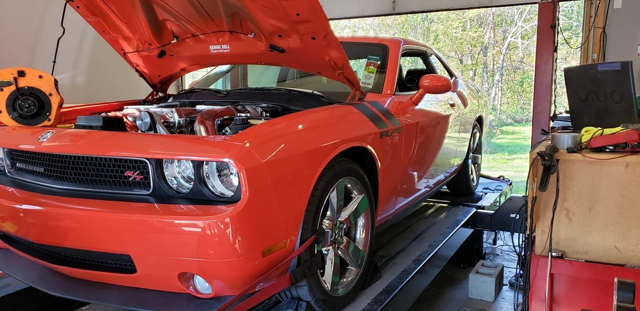 An orange dodge challenger is sitting on a lift in a garage with its hood open.