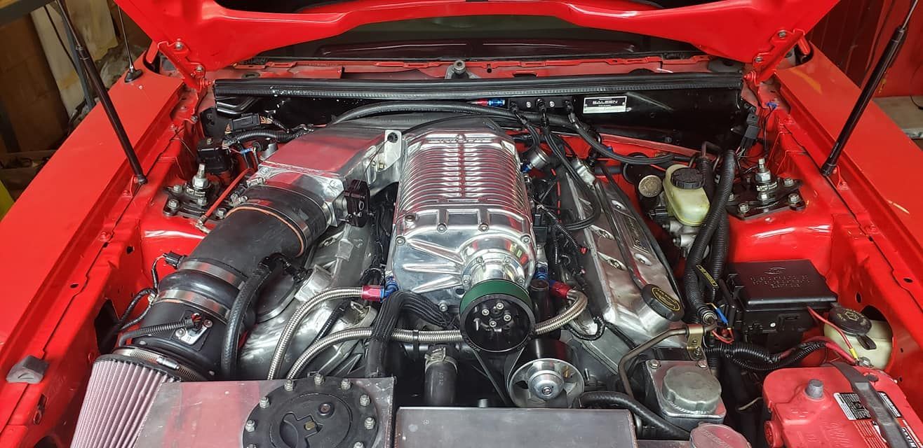 The engine of a red car is shown with the hood open.