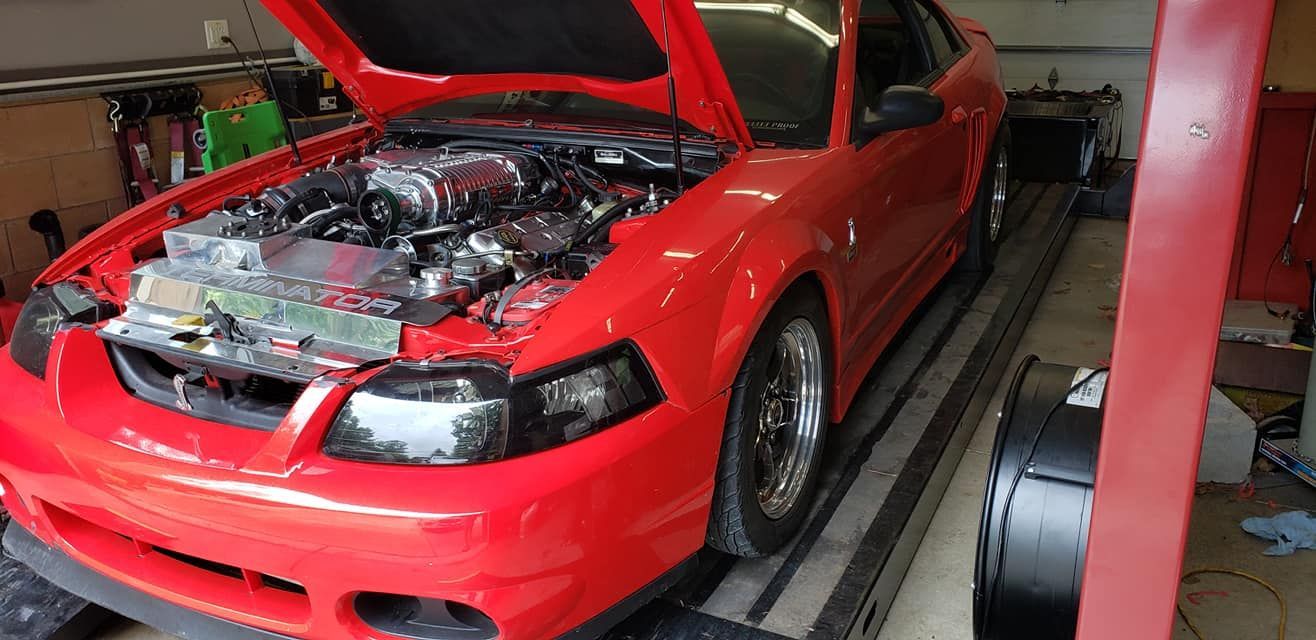 A red mustang is parked in a garage with the hood up.