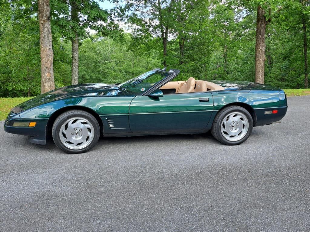 A green corvette convertible is parked on the side of a road.