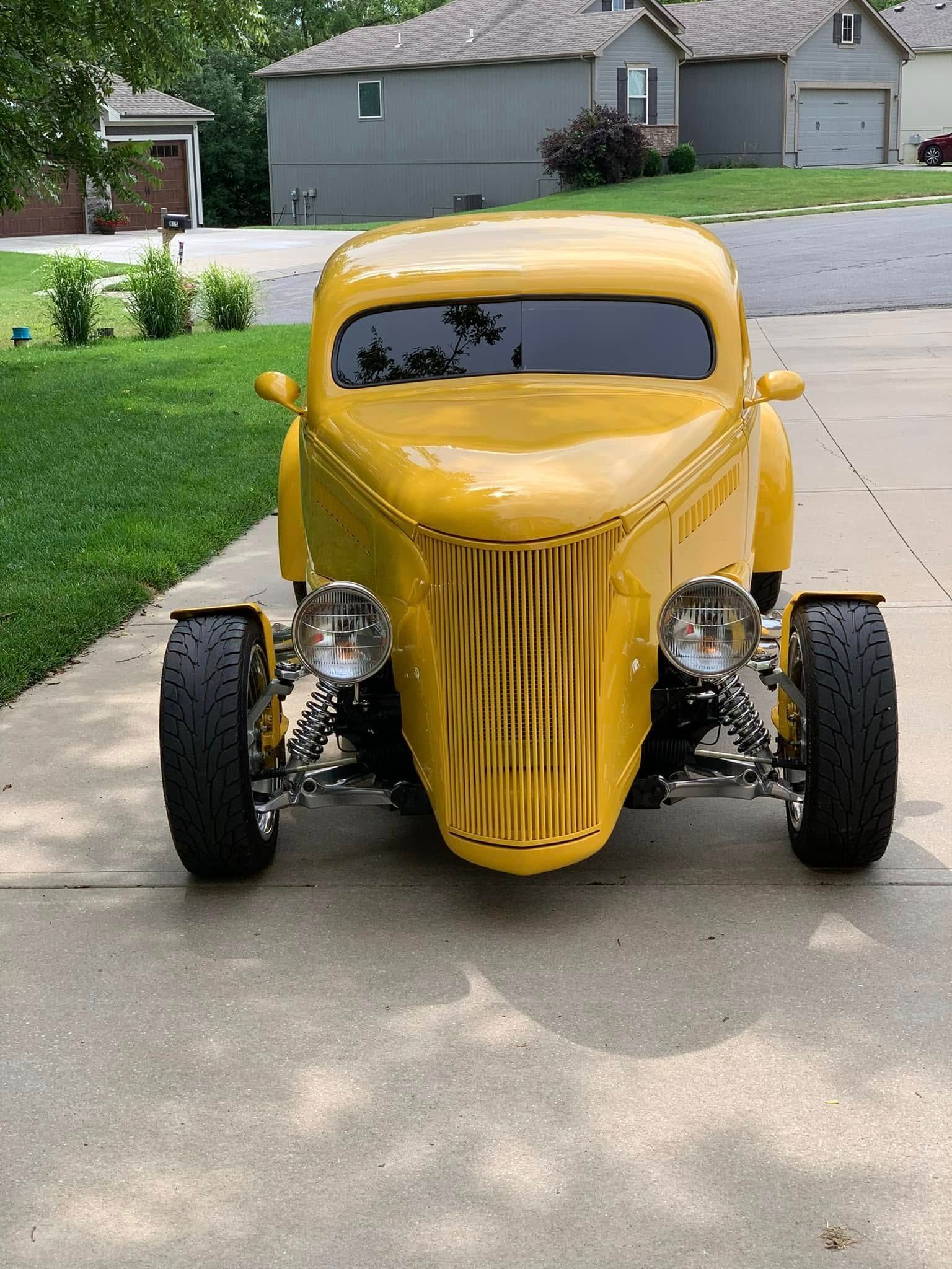 A yellow car is parked in a driveway in front of a house.
