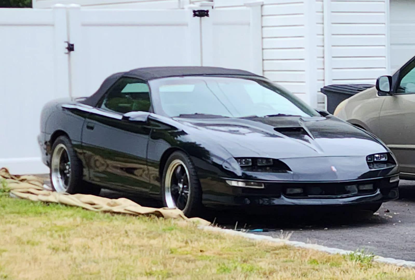 A black convertible car is parked in front of a white fence.